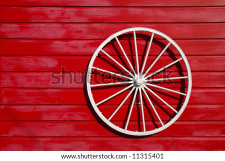 White wagon wheel is used as an ornament for a red barn.
