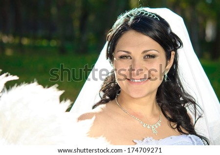 happy bride in the park. brown-eyed brunette with a white fan shape