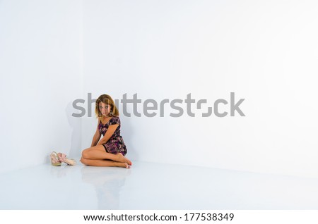sad girl sitting in the corner of a white wall. pink shoes, lilac dress