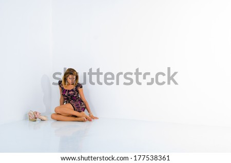 sad girl sitting in the corner of a white wall. pink shoes, lilac dress