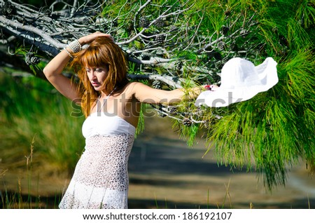 sad girl in white swimsuit with red hair near the tree on the beach