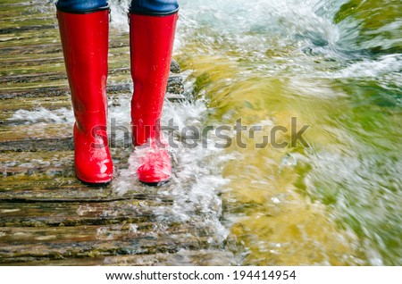 red rubber boots in water on a wooden bridge, the river overflowed its banks.