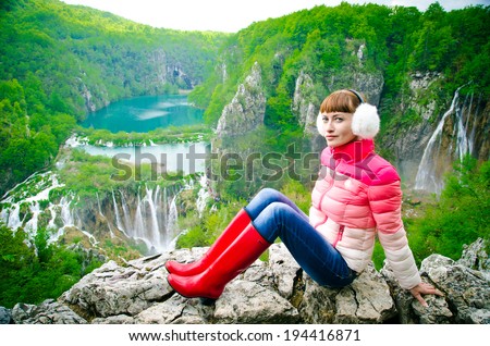 happy girl on the observation deck in bright clothes and red rubber boots. Plitvice Lakes, Croatia.
