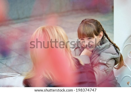 Mom and daughter sit at the table of an outdoor cafe in the fall. Conversation, sharing secrets. view through the foliage