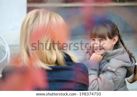 Mom and daughter sit at the table of an outdoor cafe in the fall. Conversation, sharing secrets. view through the foliage