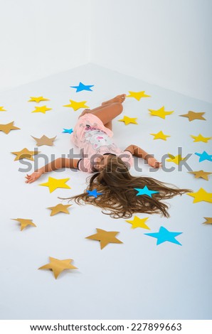 girl lying on the stars in the studio on a white background. Large colored paper stars. The magic of your own hands