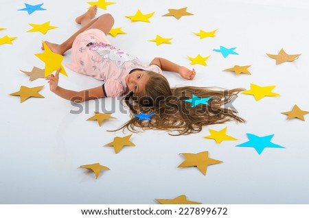 girl lying on the stars in the studio on a white background. Large colored paper stars. The magic of your own hands