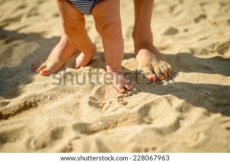 Mother and baby feet walking on sand beach