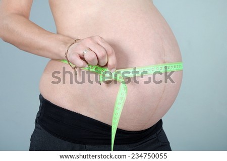 Belly of a pregnant woman with measuring tape, 9 month of pregnancy