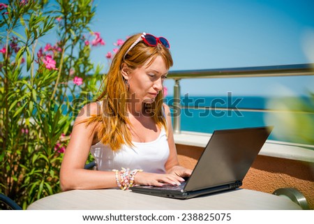 Beautiful smiling woman working on laptop. thoughtful girl working with a laptop on the terrace of the summer cafe