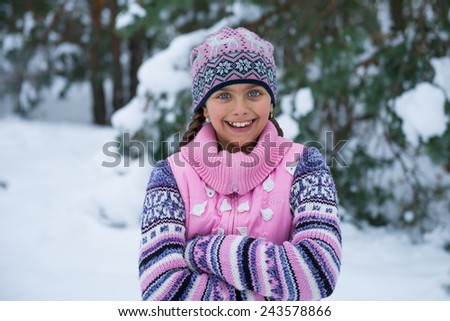 beautiful girl in winter on a background of winter nature. Happy little girl in pink sweater walking in the park