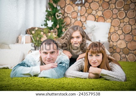 Middle-aged couple with little girl laying on carpet. family in sweaters against the background of home interior. winter portrait of a family of three