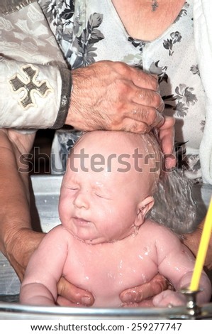 Newborn baby in font with hands of priest. baby christening. hair cutting scissors hands of the priest. Ceremony of a christening in Christian church