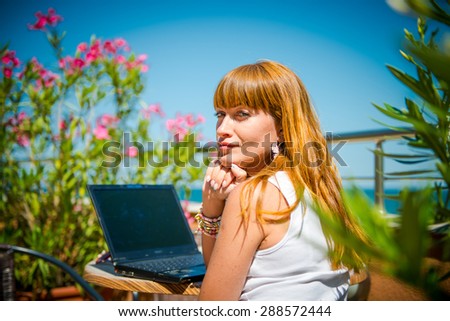 Beautiful smiling woman working on laptop. thoughtful girl working with a laptop on the terrace of the summer cafe. view in the back