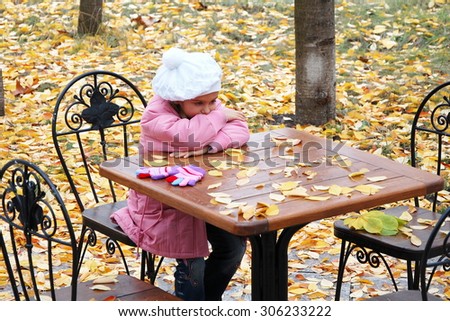 sad girl in the autumn. little girl sitting alone at a table cafe. girl in a pink coat was left alone. No family, no parents. Girl waiting for mum and dad. without family