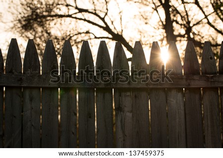 Old Fence and Sun. the sun peeks through tips of an old fence. vintage styled background