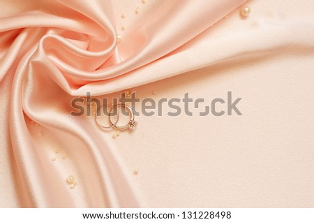 Drapery of delicate pink satin in the corner with pearls and wedding rings