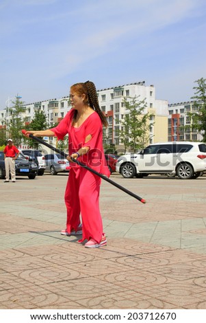 LUANNAN COUNTY - JUNE 29: woman in red performing stick fencing in the square, on june 29, 2014, LuanNan county, hebei province, China
