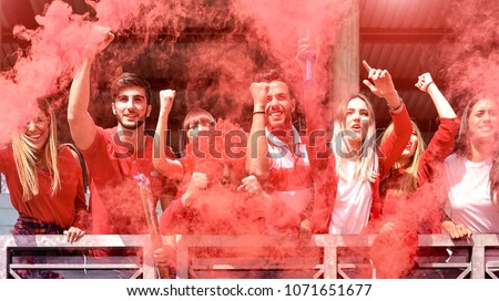 Young football supporter fans cheering with colored smoke watching soccer match together at stadium - Friends people group with red t-shirts having excited fun on sport world championship concept