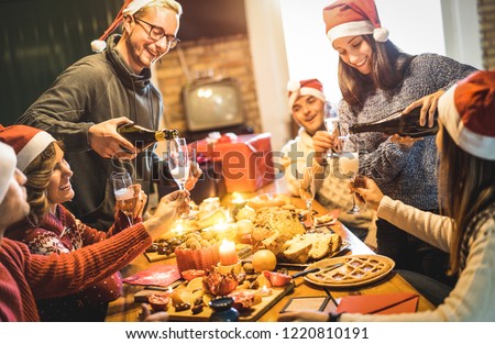 Friends group with santa hats celebrating Christmas with champagne and sweets food at home dinner - Winter holidays concept with people enjoying time and having fun eating together - Warm filter