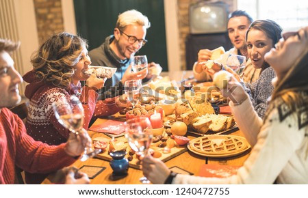 Happy young friends group tasting christmas sweet food diner having fun at home wine party - Winter holidays concept with millenial people enjoying new year's eve supper eating together - Warm filter