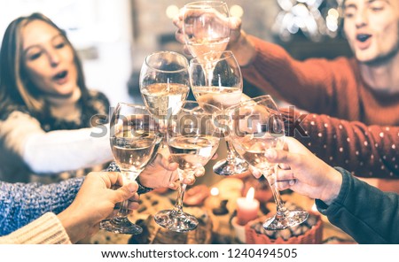 Friends group celebrating Christmas toasting champagne wine at home dinner - Winter holiday concept with young people enjoying time and having fun together - Azure vintage filter with focus on glasses