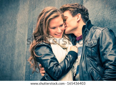 Young happy couple of lovers at beginning of love story - Handsome man whispers soft kisses in young woman ear - Fall fashion concept with boyfriend and girlfriend on a cold vintage filtered look