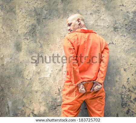 Handcuffed Prisoner in Jail waiting for Death Penalty - Guantanamo orange clothes - Grunge dramatic wall background