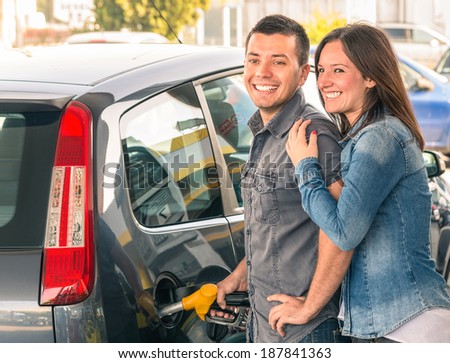 Happy couple at fuel station pumping gasoline at gas pump. Portrait of young man and woman of man filling modern car at gasoline tank.