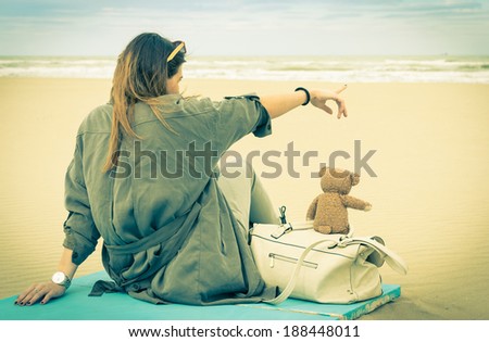 Young single woman sitting at the beach with her teddy bear looking at the sea - Vintage retro nostalgic filtered look