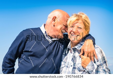 Happy senior couple in love during retirement - Joyful elderly lifestyle with man whispering and smiling with her wife