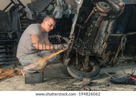 Young mechanical worker repairing an old vintage car body in messy garage