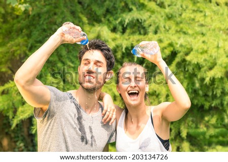 Sporty couple refreshing with cold water after run training in the park - Sport fitness young happy models taking a break after jogging in the nature