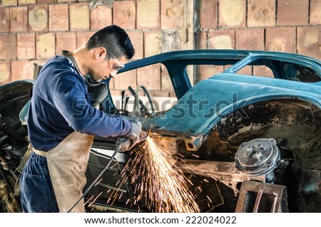 Young man mechanical worker repairing an old vintage car body in messy garage - Safety at work with protection wear
