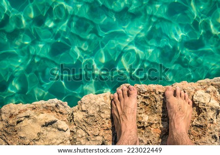 Naked human barefoot on rock cliff ready to jump in the clear blue water - Comino and Gozo blue lagoon in Malta - Freedom and carefree lifestyle during travel and vacation in exclusive destinations