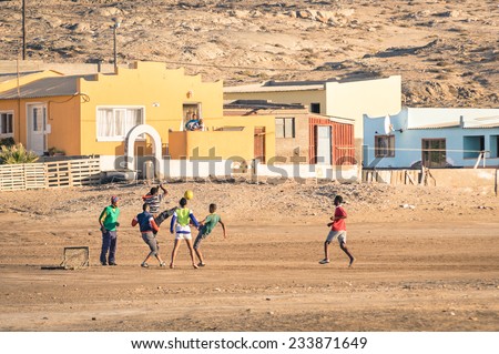 LUDERITZ, NAMIBIA - 24 NOVEMBER 2014: local young people playing football in the playground next to a modern township; for lucky and talented players, soccer is a fast way to escape poverty of slums