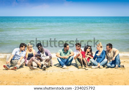 Group of international best friends sitting at beach talking with each other - Concept of multi cultural friendship against racism - Interaction with new technologies tablet and contact with nature