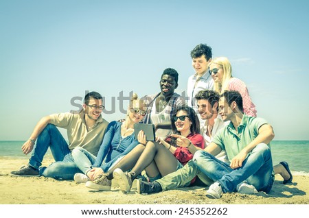 Group of young hipster best friends with digital tablet sitting at the beach - Concept of multi cultural friendship and social media networking - Interaction with new trends and technology devices