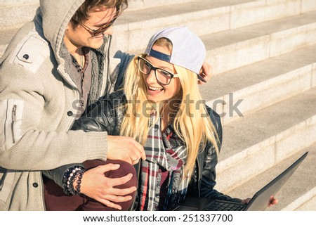 Couple of young hipster people with computer laptop in urban location outdoors - Concept of interaction and fun with new trends and technology - Wireless connection and web internet social networking