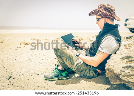 Young hipster man sitting in desert road - Concept of modern technologies with a alternative travel lifestyle - Overexposed vintage desaturated filtered look with focus on the hand using the laptop