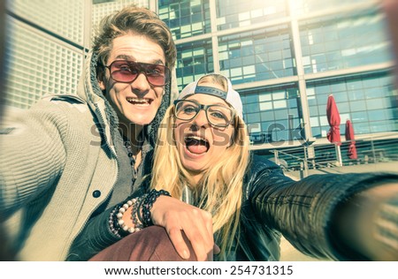 Young hipster couple in love taking a funny selfie in urban city background - Alternative concept of fun and interaction with new trends and technology - Vintage filtered look with blurred edges