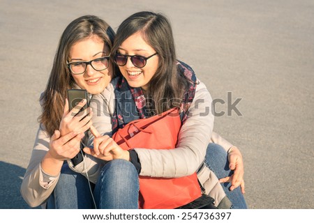 Best friends enjoying time together with smartphone in a spring sunny day - New trends and technology concept with hipster girlfriends having fun outdoors - Alternative four seasons fashion clothes
