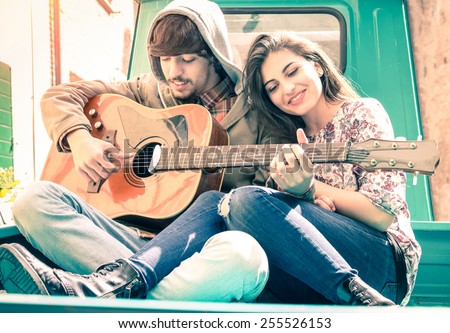 Romantic couple of lovers playing guitar on old fashioned mini car - Nostalgic retro concept of love with soft focus on the faces of boyfriend and girlfriend - Overexposed desaturated vintage filter