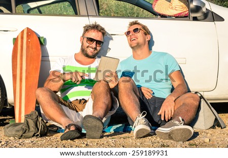 Young hipster best friends having fun with tablet during a car trip moment - Concept of modern technologies and new trends during alternative travel vacation on the road - Nostalgic sunny afternoon