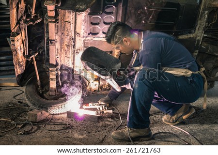 Young man mechanic worker repairing old vintage car body in messy garage - Safety at work and protection wear - Guy with cool hair cut at vehicle renovation - Soft focus with natural light lens flare