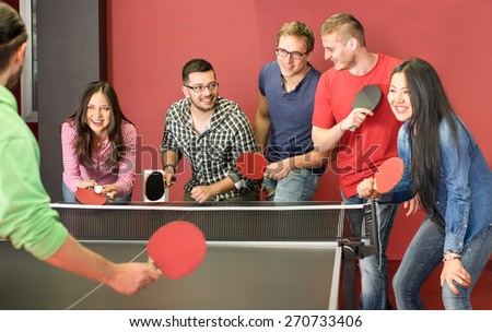 Group of happy young friends playing ping pong table tennis - Fun moment in game room of traveler youth hostel - Concept of vintage sport and genuine emotions - Main focus on two guys with eye glasses