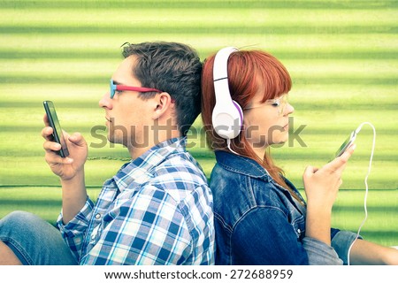 Hipster couple in disinterest moment with mobile phones - Concept of apathy sadness and isolation using new technologies - Boyfriend and girlfriend with smartphones addiction - Vintage filtered look