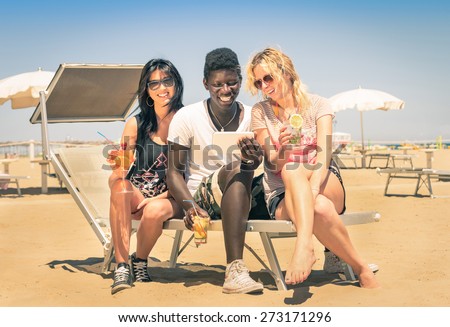 Multiracial friendship with smiling guy with girlfriends drinking cocktails with tablet pc at the beach - Modern concept of vacations with friends having fun enjoying wifi internet in the summer