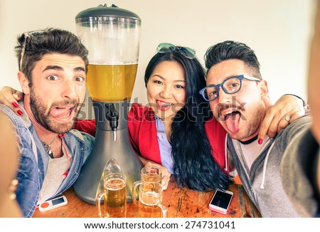 Happy friends taking selfie with funny tongue out near beer tower dispenser - Concept of friendship and fun with new trends and technology -  Alternative everyday party life in vintage brewery bar