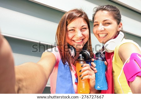 Sporty girlfriends taking phone selfie during a break at run training in urban area - Young happy women having fun together with fitness jogging workout - Fashion sport clothes and energetic drinks